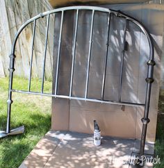 an iron bed frame with a spray bottle on the ground next to it and a wall behind it