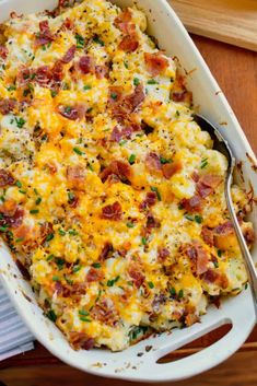 a casserole dish with bacon and cheese in it on a wooden table next to a fork