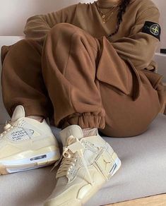 a man sitting on the floor with his feet up and wearing brown sweatpants, white sneakers