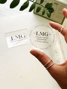 a person holding up a clear round object with the word lmg on it in front of a plant