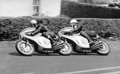 two men riding motorcycles down the street in black and white