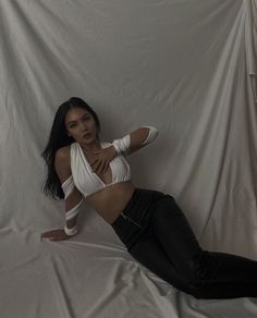 a woman laying on top of a white sheet covered bed wearing black pants and heels