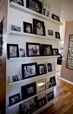 a wall filled with lots of pictures and framed photos next to a wooden floor in front of a doorway