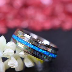 two wedding bands with blue opal inlays are sitting next to white flowers