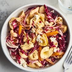 a white bowl filled with pasta and veggies on top of a marble table