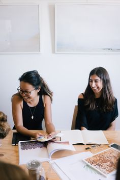 two young women sitting at a table with books and papers on top of the table