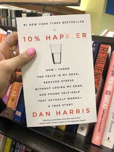 a person holding up a book in front of bookshelves with the title 10 % happier on it