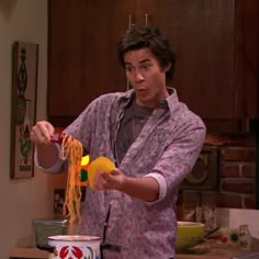 the young man is making pasta in his kitchen, while holding it with one hand