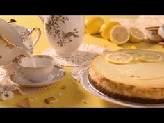 a table topped with a cake covered in lemons next to cups and saucers