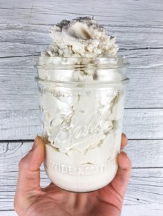 a hand holding a mason jar filled with whipped cream