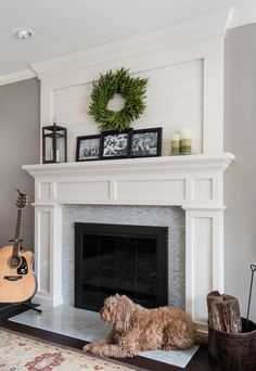 a dog laying on the floor in front of a fireplace with a wreath above it