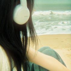 a woman sitting on the beach with headphones in her ear and looking at the ocean