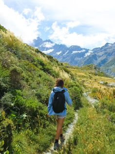 a woman walking up a trail in the mountains with a backpack on her back,