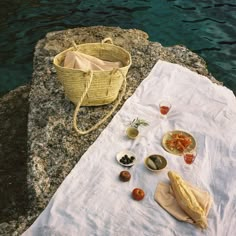 a table with food on it next to the water and a picnic blanket in front of it