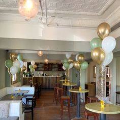 a room filled with tables and chairs covered in white, gold and green balloon decorations