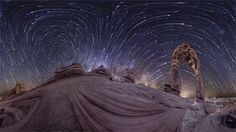 the night sky is filled with star trails and stars above rocks, in front of a large rock formation