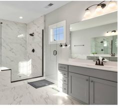 a white bathroom with marble counter tops and gray cabinets, along with a walk - in shower