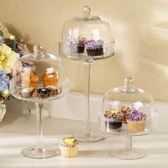 cupcakes and muffins under glass dome on table next to flower arrangement