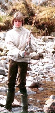 a woman is standing in the water holding a fishing rod and wearing boots with rubber boots