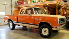 an orange pick up truck parked in a garage next to other trucks and tools on the shelves