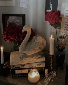 a swan figurine sitting on top of books next to candles and some roses