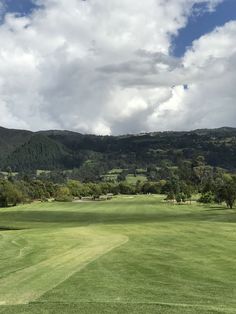 a green golf course with mountains in the back ground and clouds in the sky above