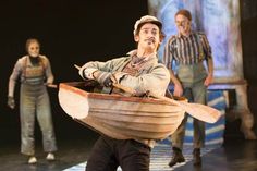 a man carrying a wooden boat on top of a stage with other people in the background