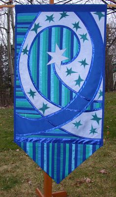 a blue and white banner hanging from a wooden stand in the grass with trees behind it