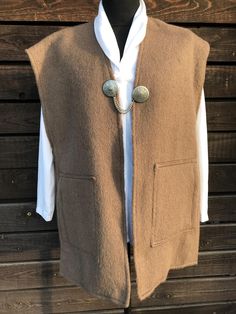 A long folk-style woollen waistcoat in a very nice brown colour, similar to cocoa. The waistcoat is fastened with a single decorative metal buckle at the front, which has a chain on either side of the waistcoat. There are two large pockets at the sides. The waistcoat is long, warm and unlined. A great gift to keep yourself or a loved one warm. Material: wool. Size: no size label, most will fit true to size EU 42, UK 14, XL (X Large). Please also check the measurements at the bottom: MEASUREMENTS Vintage Brown Sweater Vest For Fall, Brown Buttoned Vest For Winter, Brown Winter Vest With Buttons, Brown Buttoned Sweater Vest For Fall, Wool Sweater Vest With Buttons For Fall, Brown Wool Sweater Vest For Fall, Brown Wool Vest For Workwear, Brown Wool Vest For Work, Classic Brown Vest For Winter