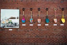 four shovels hanging on a brick wall in front of a photo and other items