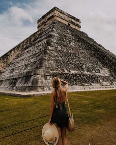 a woman standing in front of an ancient pyramid with a straw hat on her head