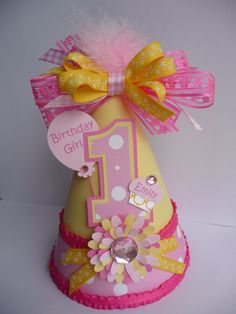 a pink and yellow birthday hat with a number one on it's side, decorated with flowers