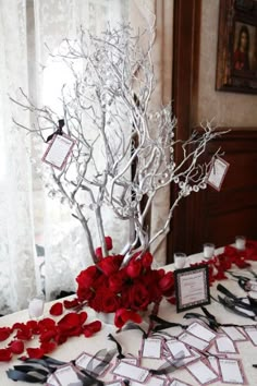 a table topped with red flowers and place cards on top of a white table cloth