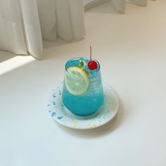 a blue drink with a slice of lemon and a cherry on the rim sitting on a white plate