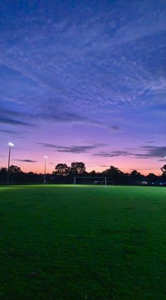 an empty soccer field at dusk with the sun setting in the distance and some lights on