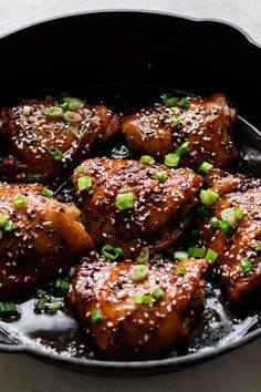 chicken with sesame seeds and green onions in a black skillet on a white surface