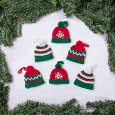 four knitted christmas hats sitting on top of a snow covered ground next to pine branches