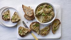 two plates with slices of bread and olives on them next to bowls of food