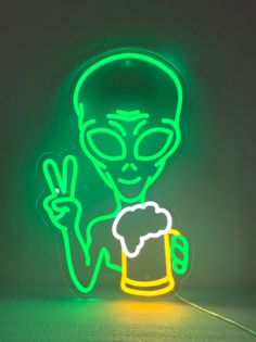 a neon sign with an alien holding a beer in it's hand and making the peace sign