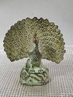 a green peacock figurine sitting on top of a white tablecloth covered floor