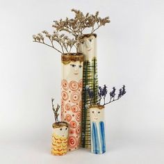 three tall vases with plants in them on a white surface, one is made out of ceramic