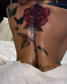 the back of a woman's body with tattoos on it and a rose tattoo