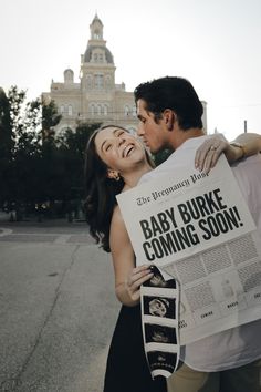 a man and woman holding up a baby burke coming soon sign in front of a building