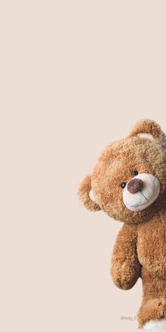 a brown teddy bear sitting on top of a white table next to a pink wall