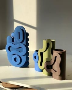 three different colored vases sitting next to each other on a white table with sunlight coming through the window