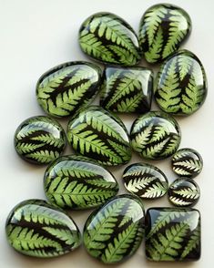 green and black leaf shaped glass cabochons on a white surface with small holes in the middle