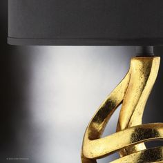 a gold lamp with a black shade on the top and bottom part, in front of a gray background