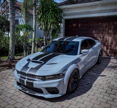 a silver and black car parked in front of a house with palm trees behind it