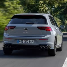 the rear end of a silver volkswagen suv driving down a road with trees in the background