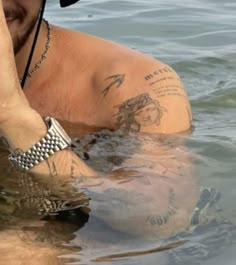 a man in the water with his hand up to his face while wearing a hat